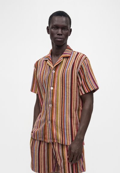 Homme portant une chemise à manches courtes et un short assorti avec des rayures verticales multicolores en rouge, orange, marron, bleu et jaune.
