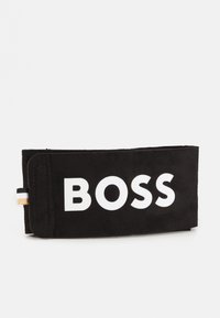 Juodas zamšas piniginė su dideliu baltu "BOSS" tekstu. Yra auksinė detalė ir juodai baltas juostelė šone.