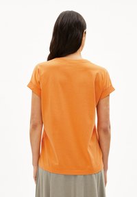 T-shirt arancione in cotone a maniche corte, con risvolti e orlo arrotondato, visto da dietro. Texture liscia, vestibilità casual.