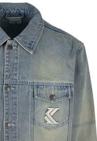 Svetlo modra jeans jakna s klasičnim ovratnikom, zapenjanjem na gumbe, sprednjim žepom in značilno logotipno nalepko na prsih.