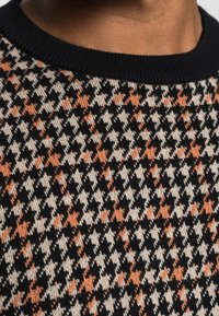 Maglione lavorato a maglia con motivo a scacchi houndstooth in nero, crema e arancione, con un colletto a costine nero solido.