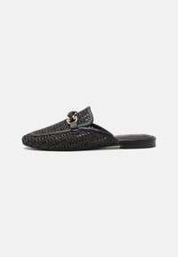Black woven slip-on shoe features a structured silhouette, leather accents, and a gold-tone decorative buckle at the front. Flat sole design.