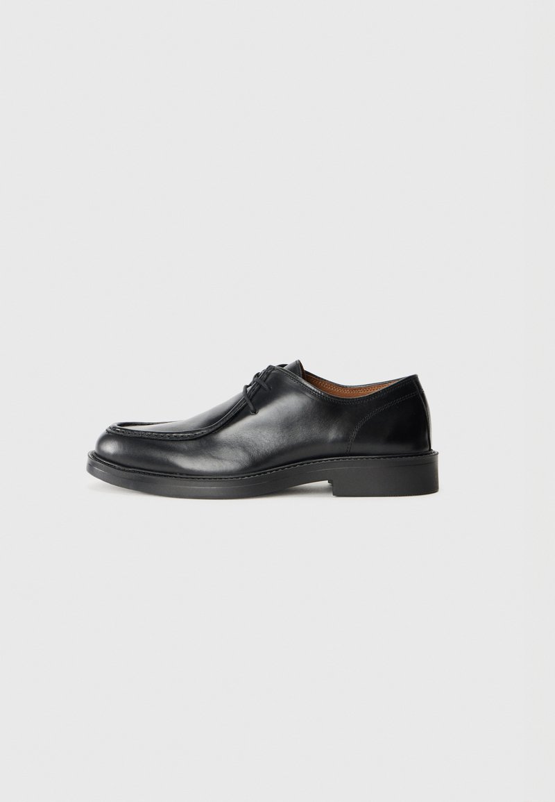Black leather dress shoe with a rounded toe, smooth surface, lace accents, and a low, textured rubber sole. Clean lines and minimal design.