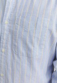 Camicia azzurro chiaro con righe bianche verticali, taschino sul petto e colletto classico; realizzata in cotone con una superficie liscia.