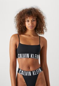 Schwarzes Bikini-Set mit einem Bralette mit dünnen Trägern und Logoband, kombiniert mit einem hochtaillierten Tanga-Bottom mit passendem Logodetail.