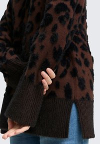 Brązowy sweter z czarnym wzorem w panterkę. Posiada ściągacze na rękawach oraz rozcięcia na dole, a także miękkie, teksturowane wykończenie.