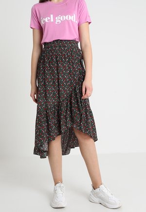 Lyserød T-shirt med hvid tekst "feel good" kombineret med en sort blomster nederdel med flæset kant og hvide sneakers.