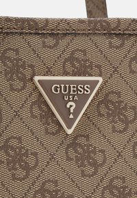 Brun mønstret mulepose med en tekstureret overflade og en trekantet metal-logo plade med "GUESS USA" og et spørgsmålstegn-design.