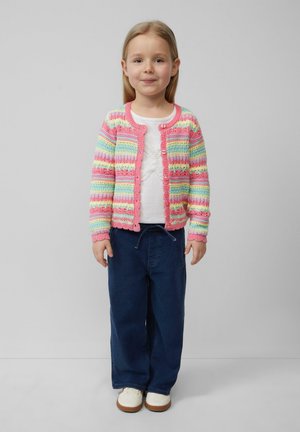 Meerkleurige gebreide cardigan met roze, blauwe en groene strepen, gecombineerd met een wit shirt en donkerblauwe wijde broek, gedragen met witte schoenen.