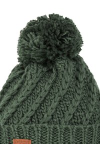 Gorro de invierno tejido en verde oscuro con patrón de trenzas, pompón grande en la parte superior y pequeña etiqueta de tela marrón en el borde.