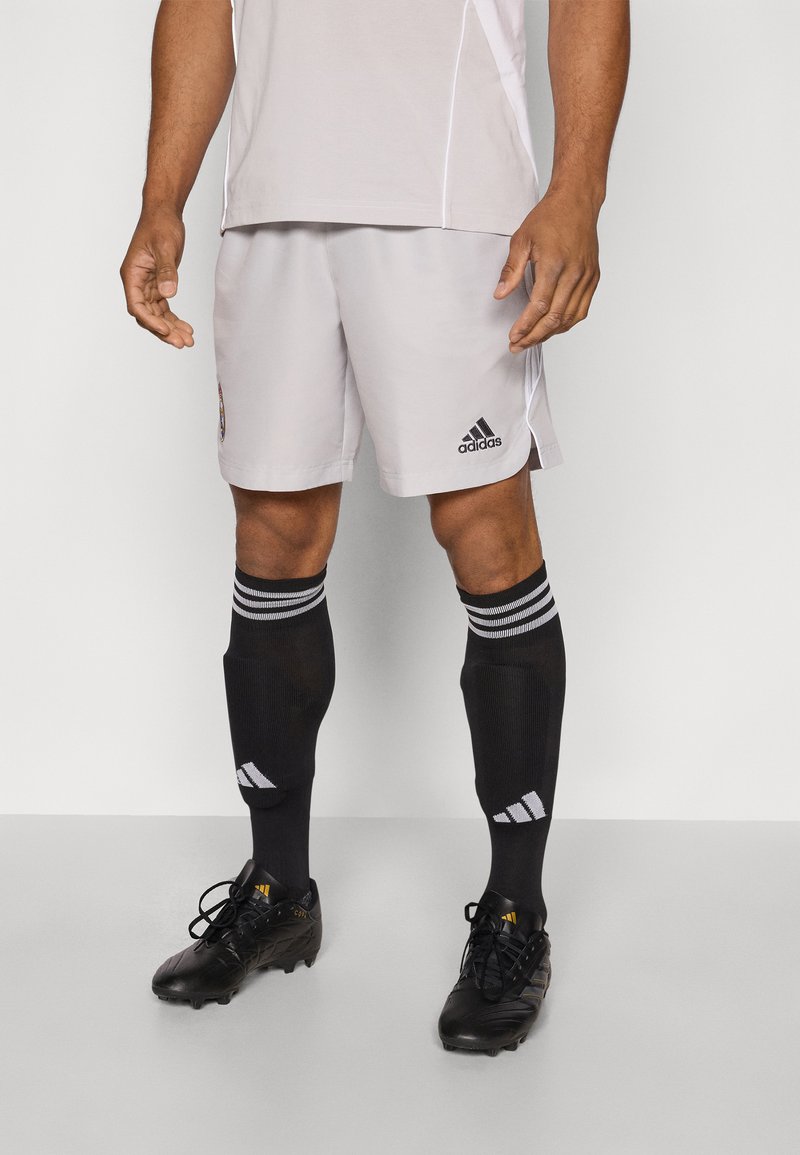 Valkoiset urheilushortsit, joissa on musta Adidas-logo, yhdistettynä mustiin polvipitkiin sukkiin, joissa on valkoiset raidat, sekä mustiin nappulakenkiin.