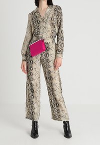 Béžová a černá halenka s hadím potiskem v kombinaci s odpovídajícími širokými kalhotami. Modelka drží malou růžovou kabelku a nosí černé boty na podpatku.