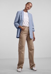 Světle modrý blazer přes bílý tričko, v kombinaci s béžovými kalhotami ve volném střihu. Bílé a šedé tenisky dokončují outfit.