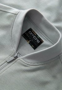Primo piano del colletto di una giacca zip-up a righe grigio chiaro con un'etichetta nera "ombre Quintessence" di taglia M all'interno.
