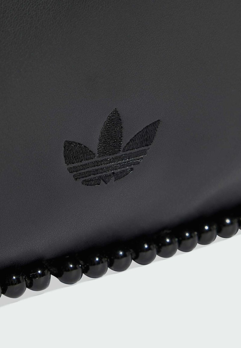 Superficie in pelle nera con logo Adidas trefoil ricamato e una fila di perle nere lucide lungo il bordo.
