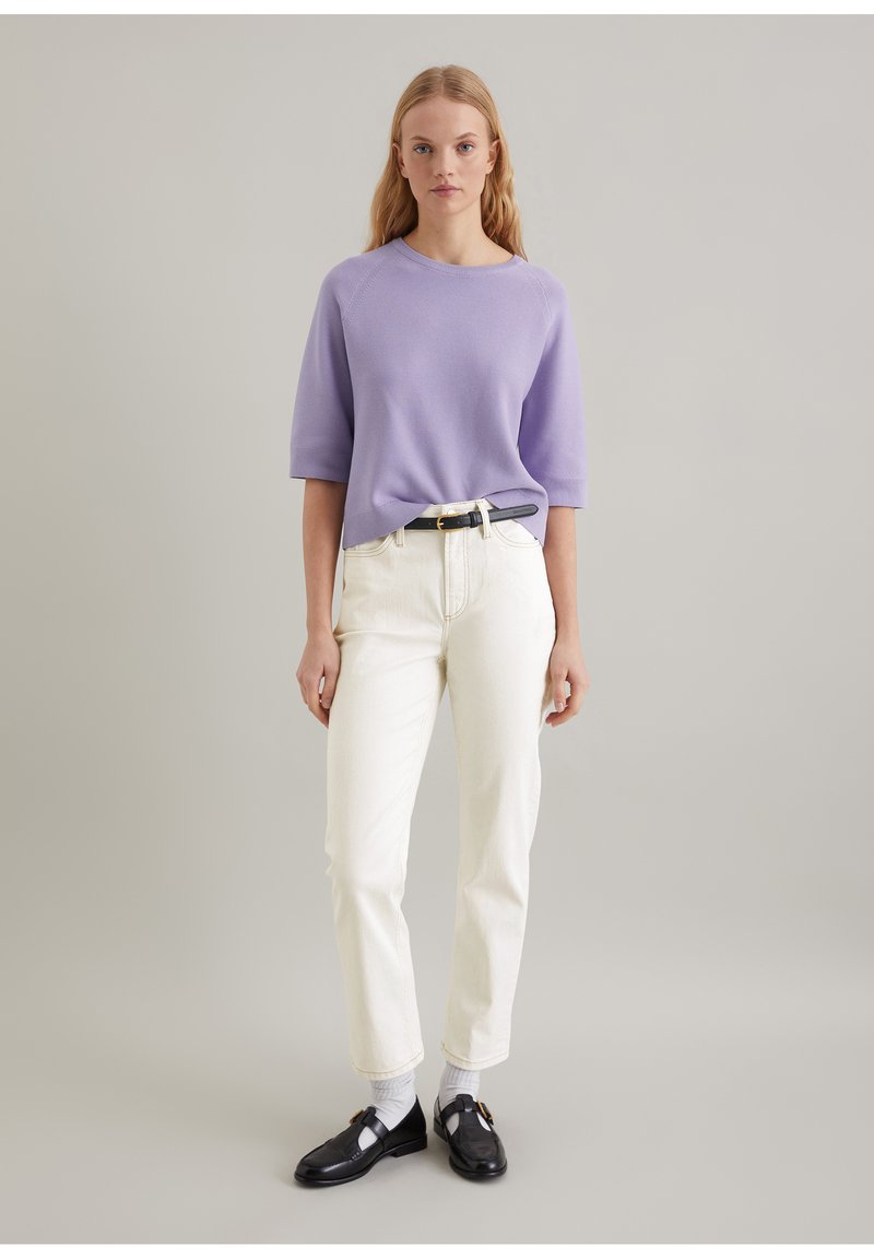 Lavendel kurzärmliger Pullover, cremefarbene gerade Jeans, schwarzer Gürtel und schwarze Schuhe mit weißen Socken. Einfaches und sauberes Design.