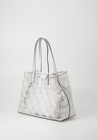 Sac fourre-tout transparent avec motif matelassé et accents de logo blancs, présentant des anses lisses et une forme structurée. Légente brillance sur le matériau transparent.