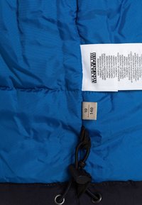 Veste matelassée bleu avec un design matelassé, comprenant un bas noir, un cordon de serrage avec un bouton-pression, et une étiquette d'entretien attachée. Étiquette de taille visible.