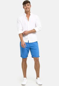 Bijela lanena košulja s gumbima, podignute rukave; plave kratke hlače s okrenutim manžetama; bijeli tenisice. Jednostavan, ležeran ljetni outfit.
