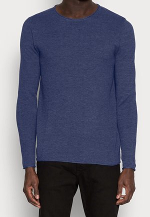Pull en tricot bleu marine à manches longues avec un col rond, en tissu texturé, coupe slim et poignets côtelés, associé à un pantalon noir.