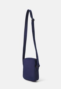 Bolso cruzado color azul marino con forma cuadrada, hecho de tela, que cuenta con un cierre de cremallera y una correa grabada con "MIS VAQUEROS TOMMY JEANS."