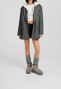 Blazer grigio oversize su una felpa bianca, pantaloni corti neri e calzini grigi arrotolati con stivaletti grigi; textures morbide e design a strati.