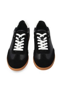 Schwarze Turnschuhe aus Leder und Wildleder. Mit weißen Schnürsenkeln und einer tanfarbenen Gummisohle. Akzentuiert mit Schwarz und Weiß am Knöchel.