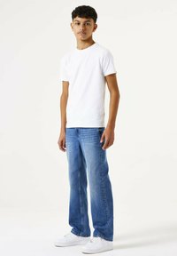 Camiseta blanca de manga corta combinada con jeans de mezclilla azul y zapatillas blancas. Jeans de corte relajado, de lavado claro y con una textura suave.