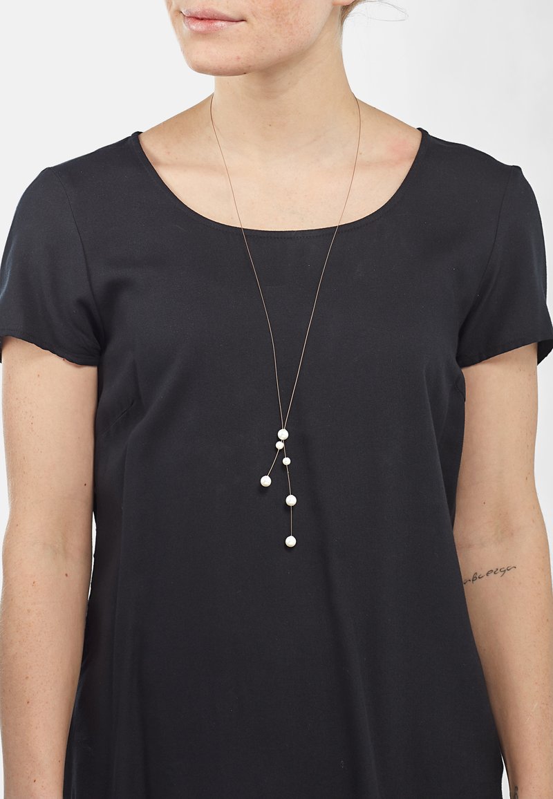 Lange, feine Halskette mit einer goldenen Kette, die mehrere weiße Perlen in unterschiedlichen Größen zeigt, die in einem kaskadierenden Design angeordnet sind.