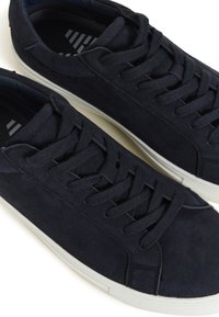 Baskets basses en daim noir avec semelles en caoutchouc blanc et lacets noirs, vues en diagonale de dessus.