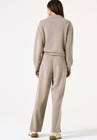Beige Sweatshirt mit herunterhängenden Schultern und passenden weiten Hosen. Weicher Stoff, elastischer Bund und Gesäßtaschen an den Hosen.
