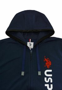 Felpa con zip di colore blu navy, dotata di cordini, con il logo di un giocatore di polo rosso e il testo "USPA" bianco sul lato destro anteriore.