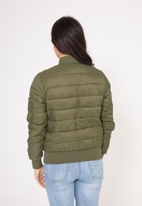 Oliwkowa, pikowana kurtka bomberka z prążkowanymi mankietami i dołem. Posiada zapinaną na zamek kieszeń na rękawie oraz gładki, lekki materiał.