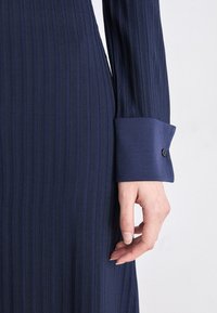 Navy blue ribbed dress with long sleeves. The cuff features a smooth texture and a button detail, highlighting a structured design.