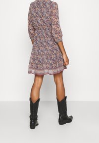 Blommönstrad klänning i mörka nyanser med trekvartsärmar, insydd midja och mönstrad fåll. Matchad med svarta cowboykängor.