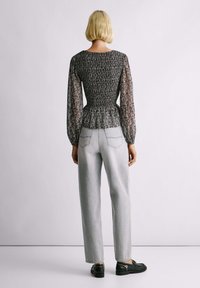 Čiernobiela blúzka s vzorom so smockovaným pásom a priesvitnými, nafúknutými rukávmi, v kombinácii s ľahkými džínsami a čiernymi topánkami.