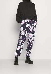 Černý strukturovaný svetr v kombinaci s květinově vzorovanými tepláky v tmavě námořnické, bílé a fialové barvě. Černé šněrovací boty dotvářejí celý outfit.