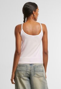 Lyserosa singlet med tynne stropper og rund hals, laget av mykt stoff. Kombinert med høy midje blå denim jeans med baklommer.