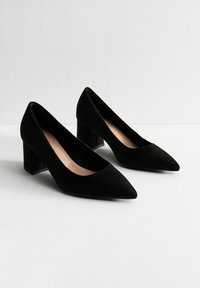 Pumps in suede nero con tacco a blocco, punta affusolata e finitura liscia e opaca. Presentano una soletta confortevole e un tacco quadrato robusto.