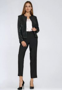 Czarna kurtka z cekinami i okrągłym kołnierzem, zestawiona z dopasowanymi czarnymi spodniami. Strój ma dopasowany krój i wysokie obcasy.