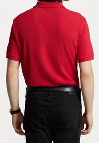 Červená polo tričko sTexturovaným povrchem, krátkými rukávy a límečkem, kombinované s černými kalhotami a černým pásem.