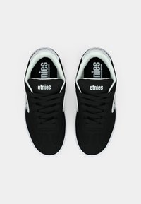 Ζεύγος μαύρων και λευκών αθλητικών παπουτσιών Etnies με κορδόνια, απεικονιζόμενο από πάνω σε ανοιχτό γκρίζο φόντο.
