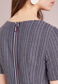 Námořnické šaty s bílými mřížkami, krátkými rukávy a zadním zipem s kruhovým táhlem. Hladká látka s mírnou strukturou.