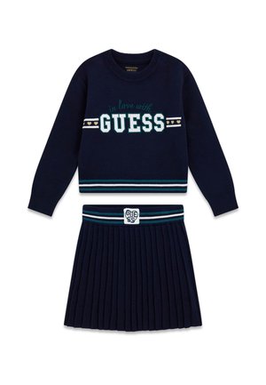 Marineblauer Pullover und plissierter Rock mit gestreiftem Rippensaum, "in love with GUESS" Schriftzug auf dem Pullover und Markenpatch am Rockbund.