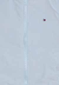 Světlomodrá bunda na zip z hladké látky, s předním zipem, malým vyšívaným logem na hrudi a boční kapsou.