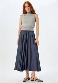 Haut sans manches gris avec ourlet côtelé, associé à une jupe fluide mi-longue bleu foncé dotée d'une taille élastique. Chaussures plates noires avec accents argentés.