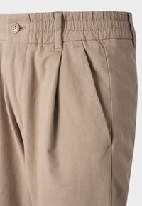 Pantalon tailleur beige en mélange de coton, doté de plis devant, fermeture à boutons et taille élastique pour le confort.