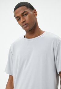 Camiseta de manga corta en gris claro, hecha de una tela texturizada, con escote redondo y un corte holgado, que presenta costuras visibles.