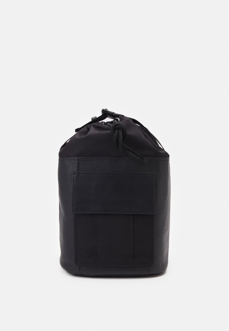 Sac à dos noir de forme cylindrique, fabriqué à partir d'un mélange de tissu et de cuir. Il dispose d'une fermeture supérieure à cordon de serrage et d'une poche plate à l'avant.