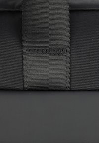 Bolsa textil negra con un diseño texturizado, área de cierre suave y una correa prominente. El material parece duradero y resistente.